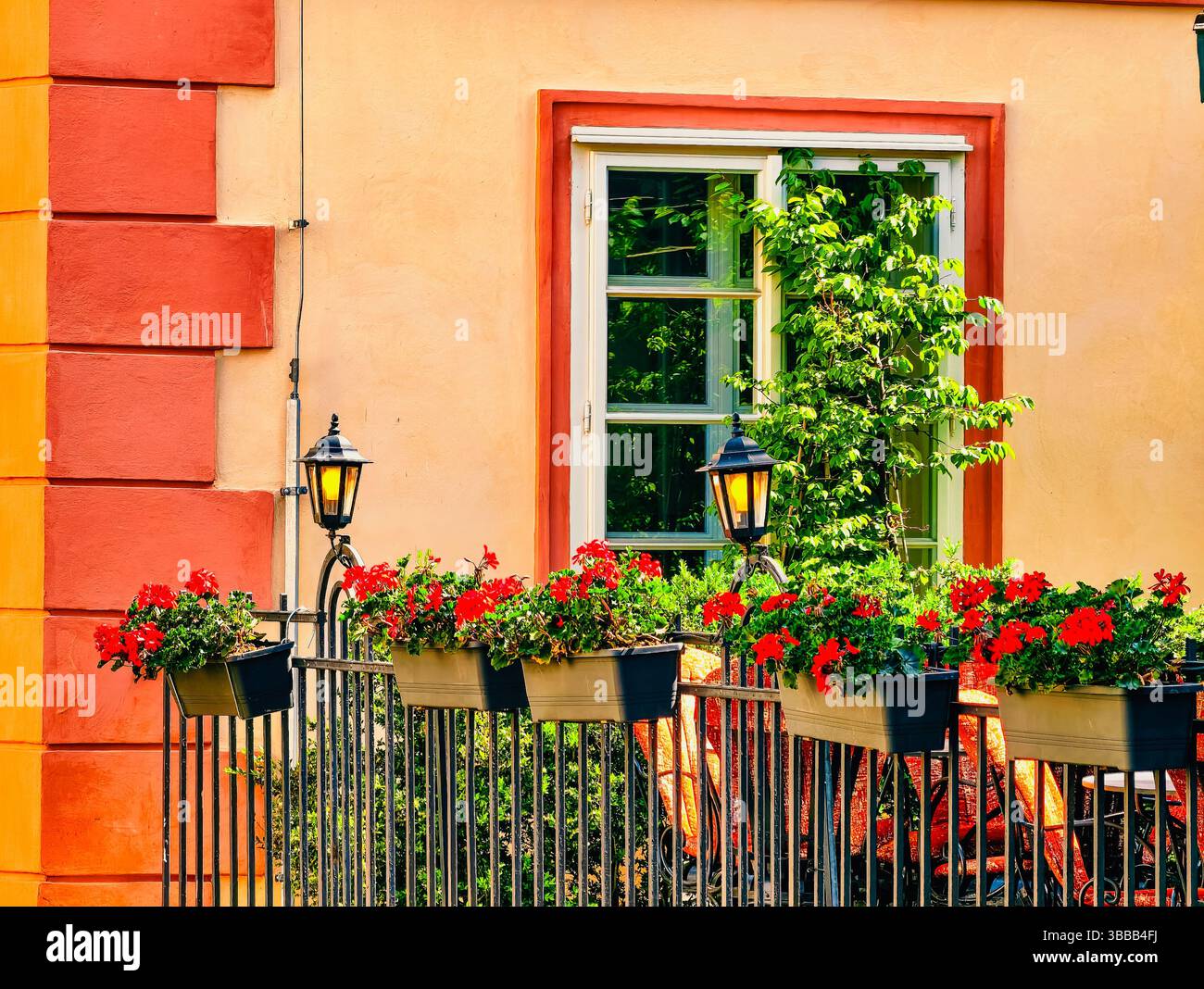 Charmanter Balkon mit leuchtenden roten Blumen und dekorativen Laternen auf einem farbenfrohen Gebäude, das eine gemütliche und einladende Atmosphäre schafft, perfekt zum Entspannen und Genießen der urbanen Schönheit Stockfoto