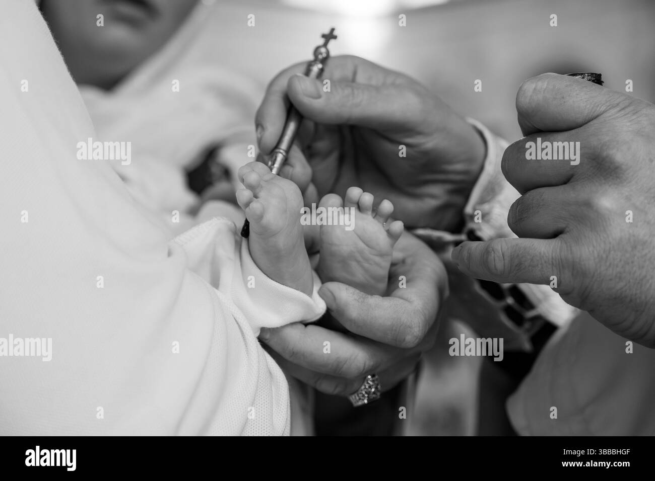 Ein zärtlicher Moment der Taufzeremonie eines Babys, bei dem die Hände eines Priesters gefangen werden, der Wasser über die Füße des Säuglings gießt, was die spirituelle Reinigung und symbolisiert Stockfoto