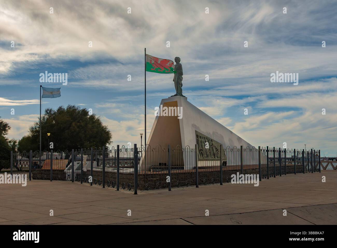 Argentinische und walisische Flaggen fliegen an einem Denkmal für walisische Pioniere in Puerto Madryn, Argentinien. Es zeigt eine walisische Frau, die auf das Land und die Zukunft blickt. Stockfoto
