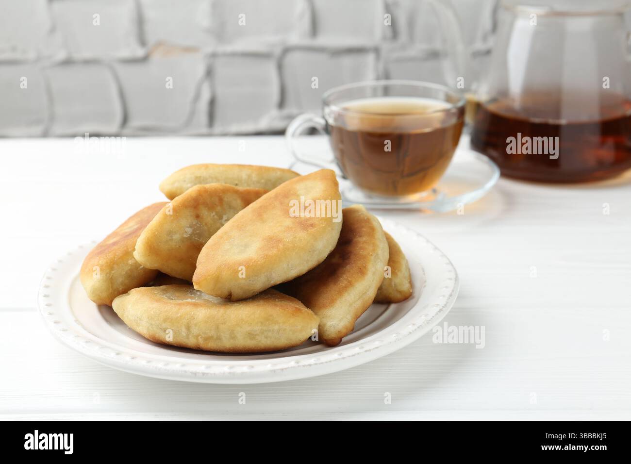 Köstliche gebratene Pyrizhky (gefüllte Kuchen) und Tee auf weißem Holztisch, Nahaufnahme Stockfoto Köstliche gebratene Pyrizhky (gefüllte Kuchen) und Tee auf weißem Holztisch, Nahaufnahme Stockfoto