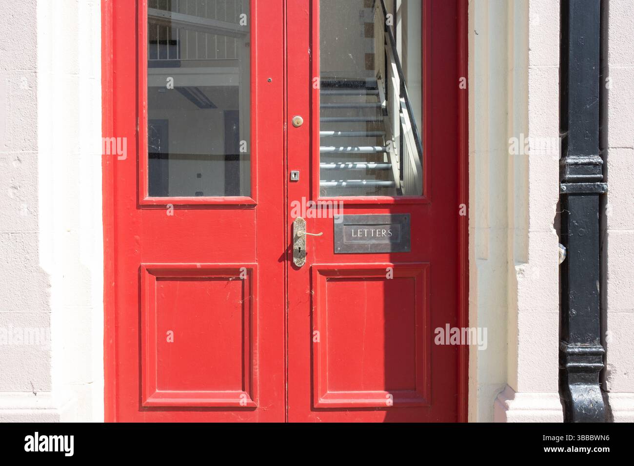 Glenarm, Nordirland - 14. Mai 2025 - lebendige, altmodische rote Tür mit schickem Briefkasten und TEXTBUCHSTABEN, Fassade des alten Gebäudes Stockfoto