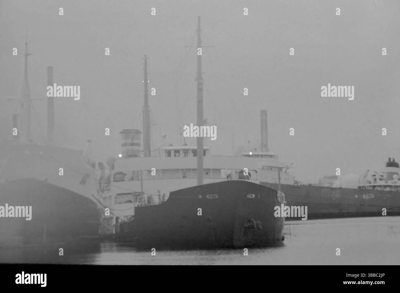 Große Seen Frachtschiffe, die im Nebel im Hafen ankern, in Schwarz-weiß mit leuchtenden Lichtern. Stockfoto