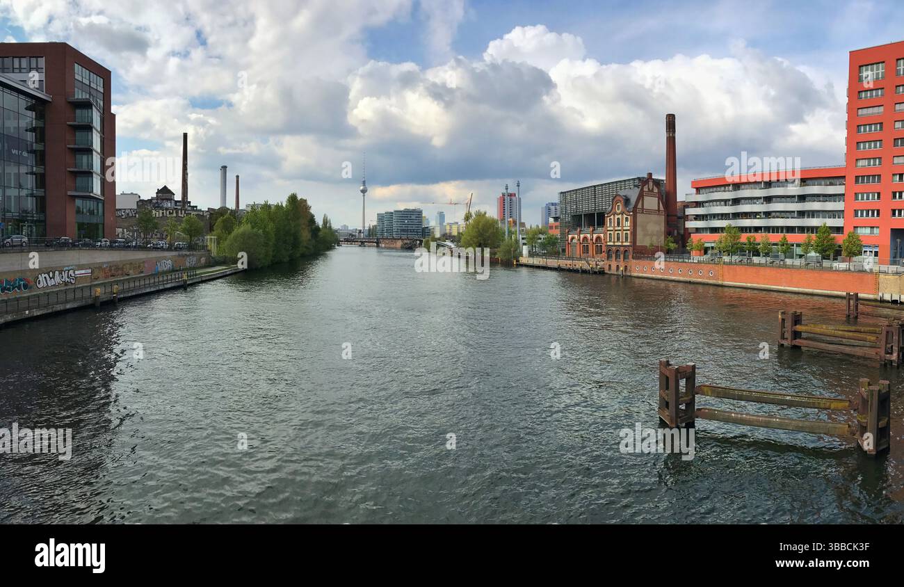 Panoramablick auf einen städtischen Fluss, umgeben von modernen Gebäuden, historischen Gebäuden und üppigen Bäumen unter bewölktem Himmel, geeignet für Header oder banne Stockfoto