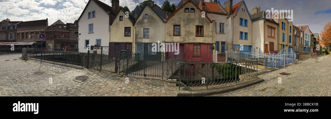 Panoramablick auf eine malerische Stadtstraße, gesäumt von bunten Häusern und Kopfsteinpflaster unter einem dramatischen bewölkten Himmel. Eine malerische Szene, die verkörpert Stockfoto