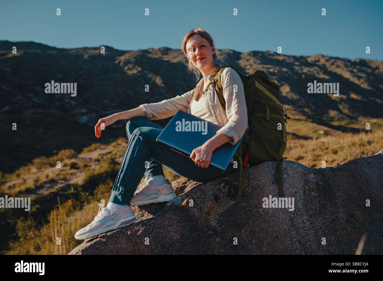 Auf dem Berg sitzt eine junge Touristin mit Rucksack und Laptop Stockfoto