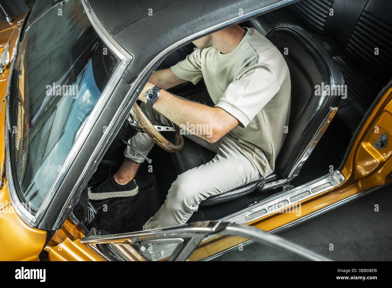 Eine Person sitzt in einem Oldtimer und greift das Lenkrad. Die Person trägt ein lässiges Outfit, das einen Sinn für Stil vermittelt. Sonnenlicht Stockfoto