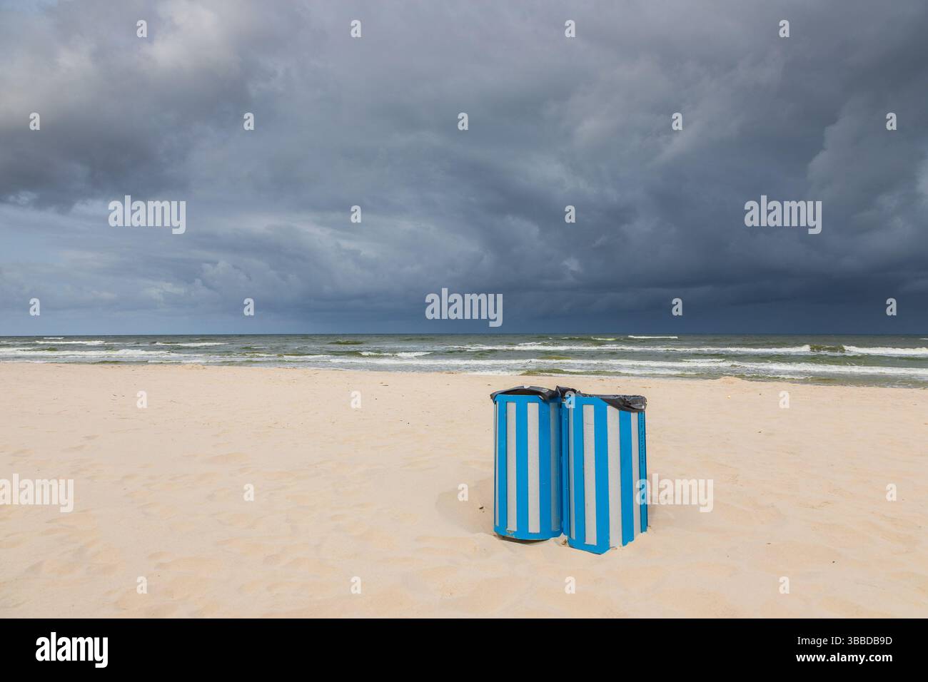 Zwei blau gestreifte Mülltonnen an einem einsamen Strand in Karwia, Polen, mit dramatischen Sturmwolken über der Ostsee. Stockfoto