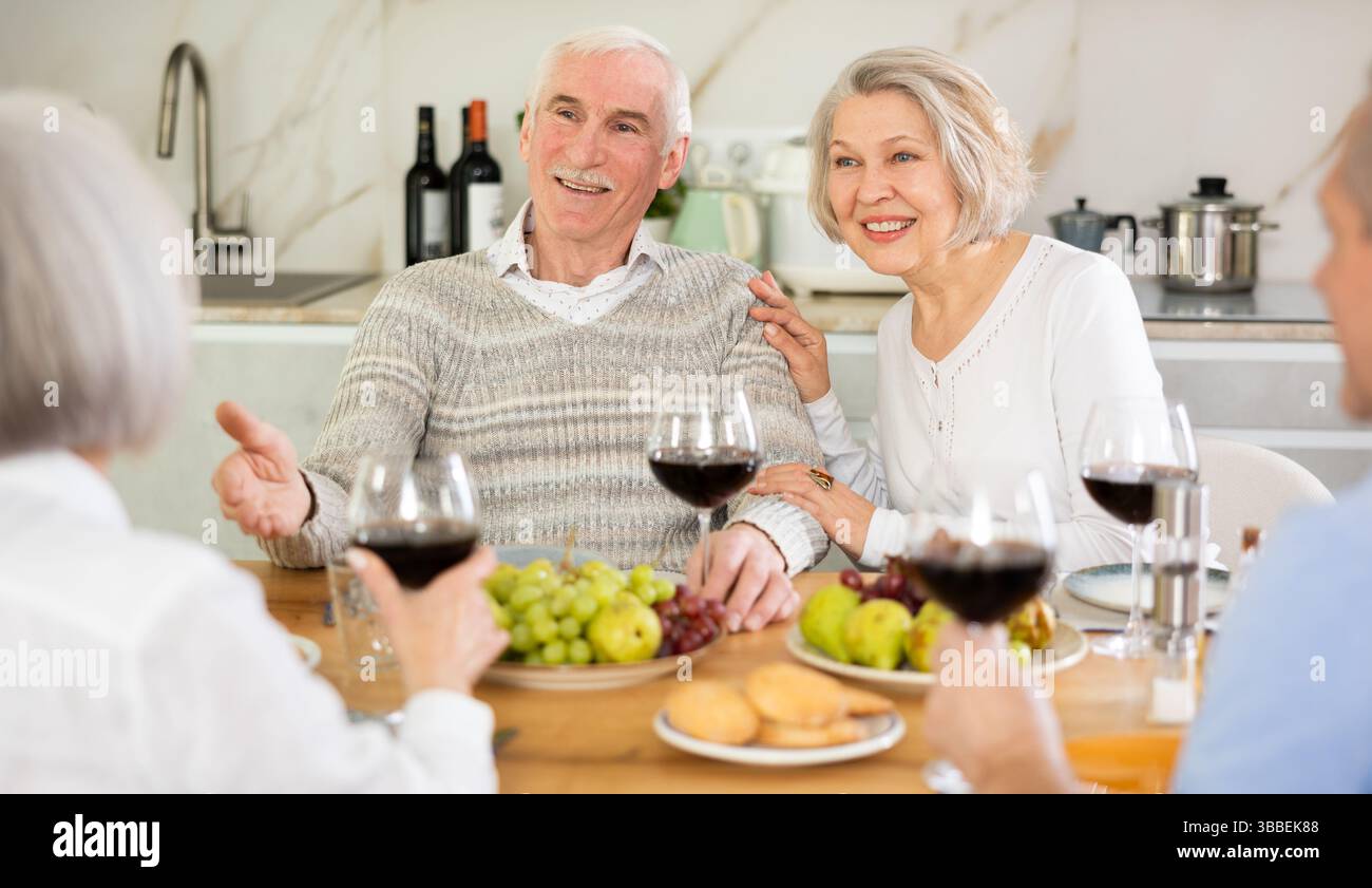Zwei ältere Ehepaare sitzen am Tisch, genießen Essen und Wein, plaudern. Stockfoto