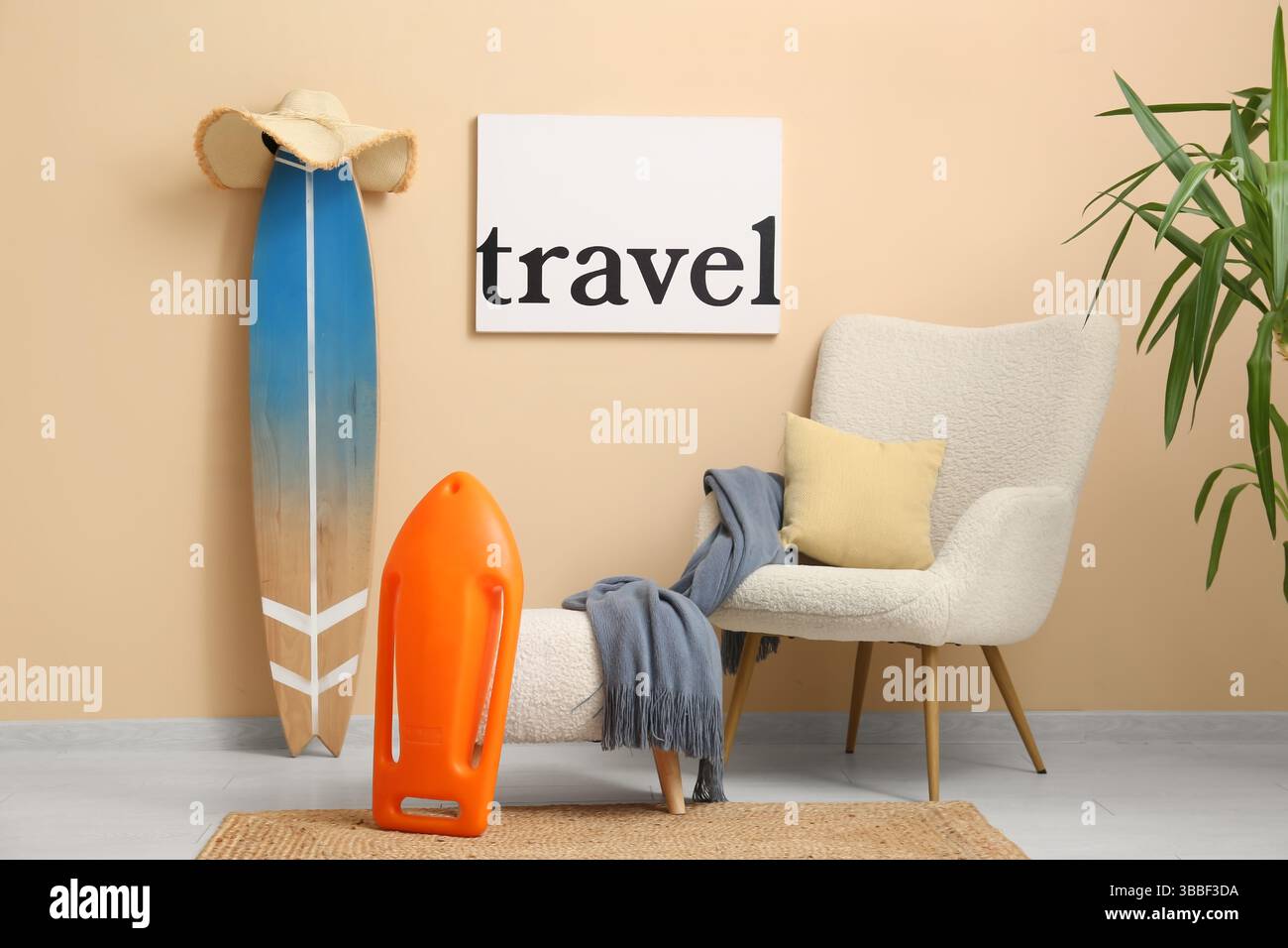 Inneneinrichtung des stilvollen Wohnzimmers mit weißem Sessel, Schwimmbrett, REISEPOSTER und Surfbrett Stockfoto