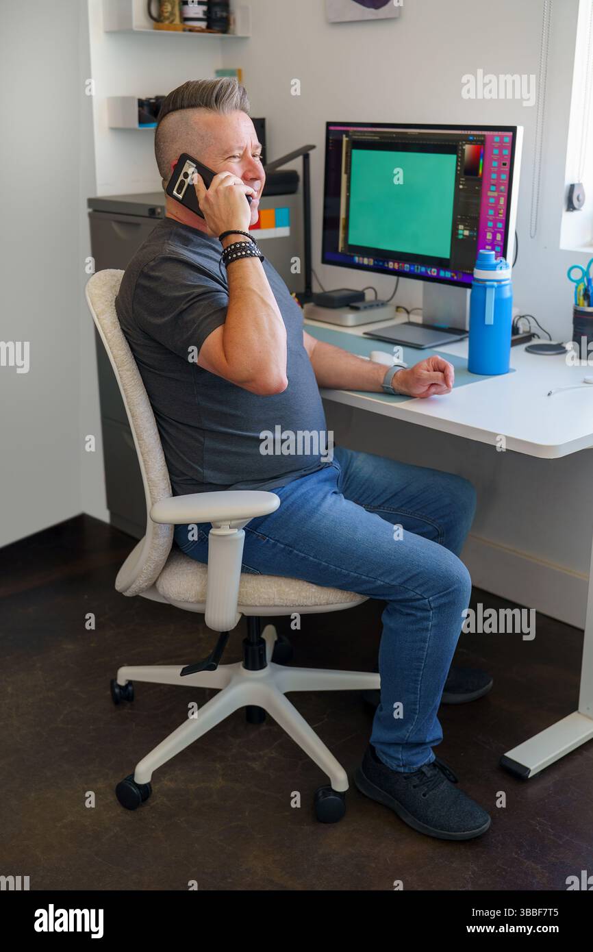 Mann, der am Schreibtisch sitzt und über das Smartphone spricht, von zu Hause aus arbeitet Stockfoto