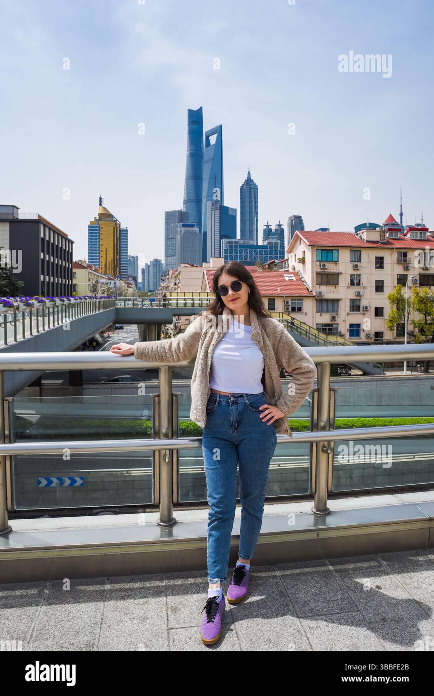 Brünette in Sonnenbrille lächelt in die Kamera auf dem Shanghai Viadukt mit Pudong Skyline mit Shanghai Tower, World Financial Center und Jin Mao Tower beh Stockfoto