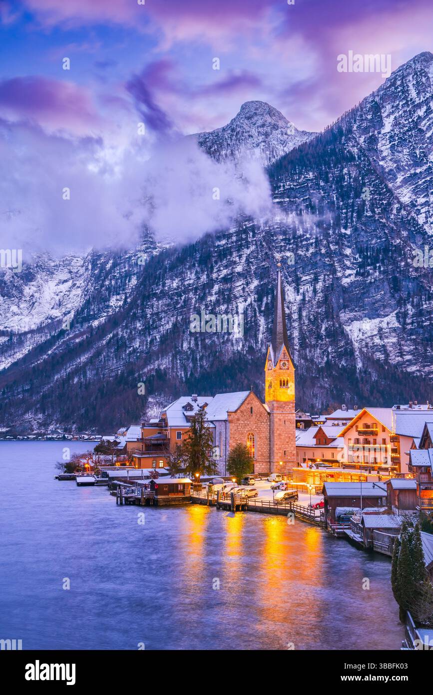Hallstatt, Österreich. Ruhiges Alpendorf mit einem ruhigen See, schneebedeckten Dächern und einer atemberaubenden Bergkulisse während der Winterdämmerung. Stockfoto