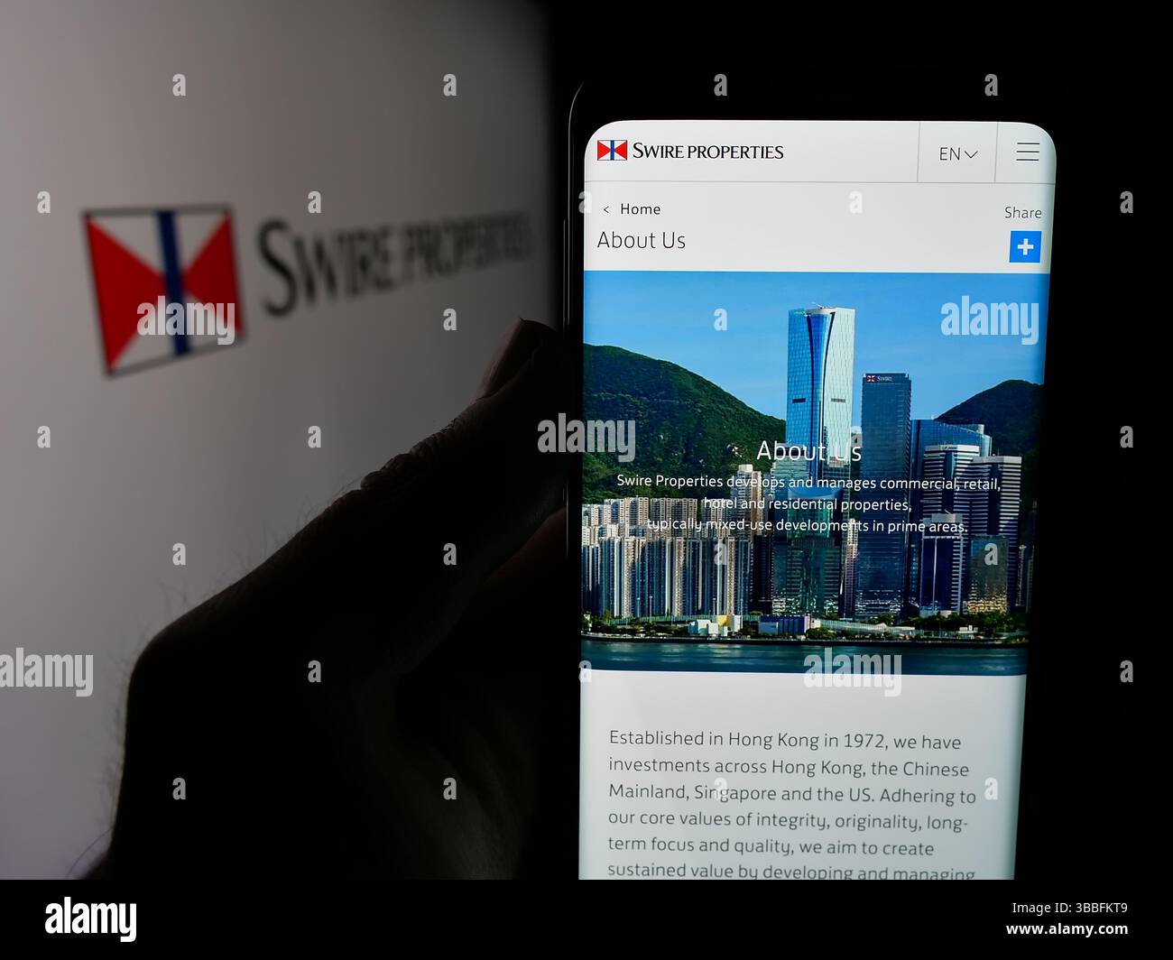 In dieser Abbildung hält eine Person ein Handy mit der Webseite des Immobilienunternehmens Swire Properties Limited auf dem Bildschirm vor dem Logo. Stockfoto