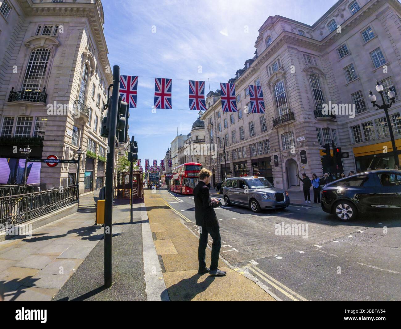 Geschäftsmann mit Smartphone auf einer londoner Straße, die mit britischen Flaggen verziert ist, mit einem typischen roten Bus und einem schwarzen Taxi im Hintergrund Stockfoto