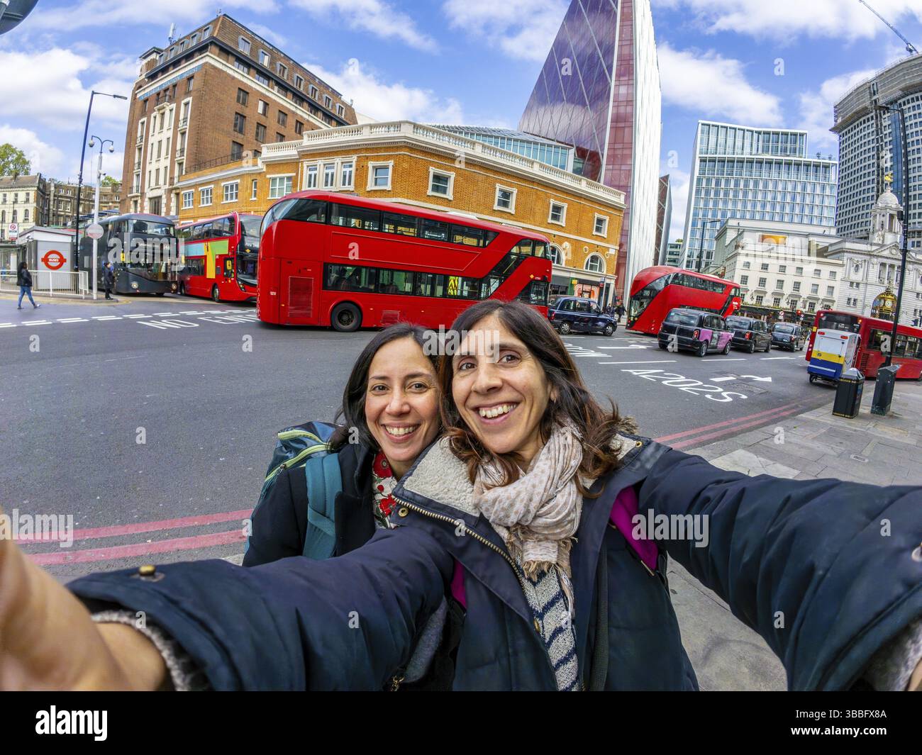 Zwei glückliche weibliche Touristen, die ein Selfie mit roten Doppeldeckerbussen und modernen Wolkenkratzern im Hintergrund machen, genießen ihren Urlaub in london Stockfoto