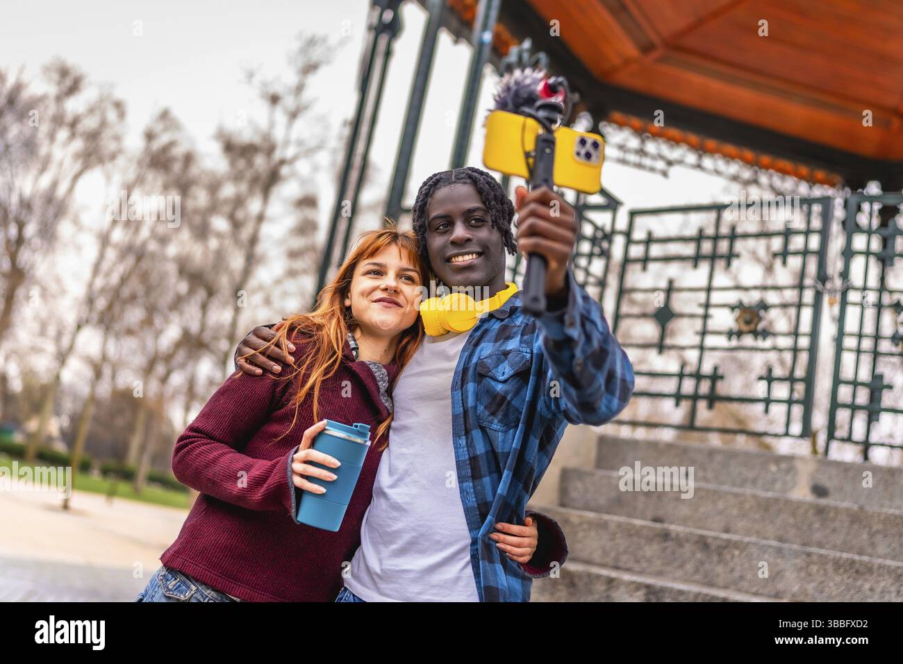 Zwei junge Content-Ersteller nehmen in einem Park einen Video-Blog auf, indem sie ein Smartphone verwenden, das an einem Gimbal mit externem Mikrofon befestigt ist Stockfoto