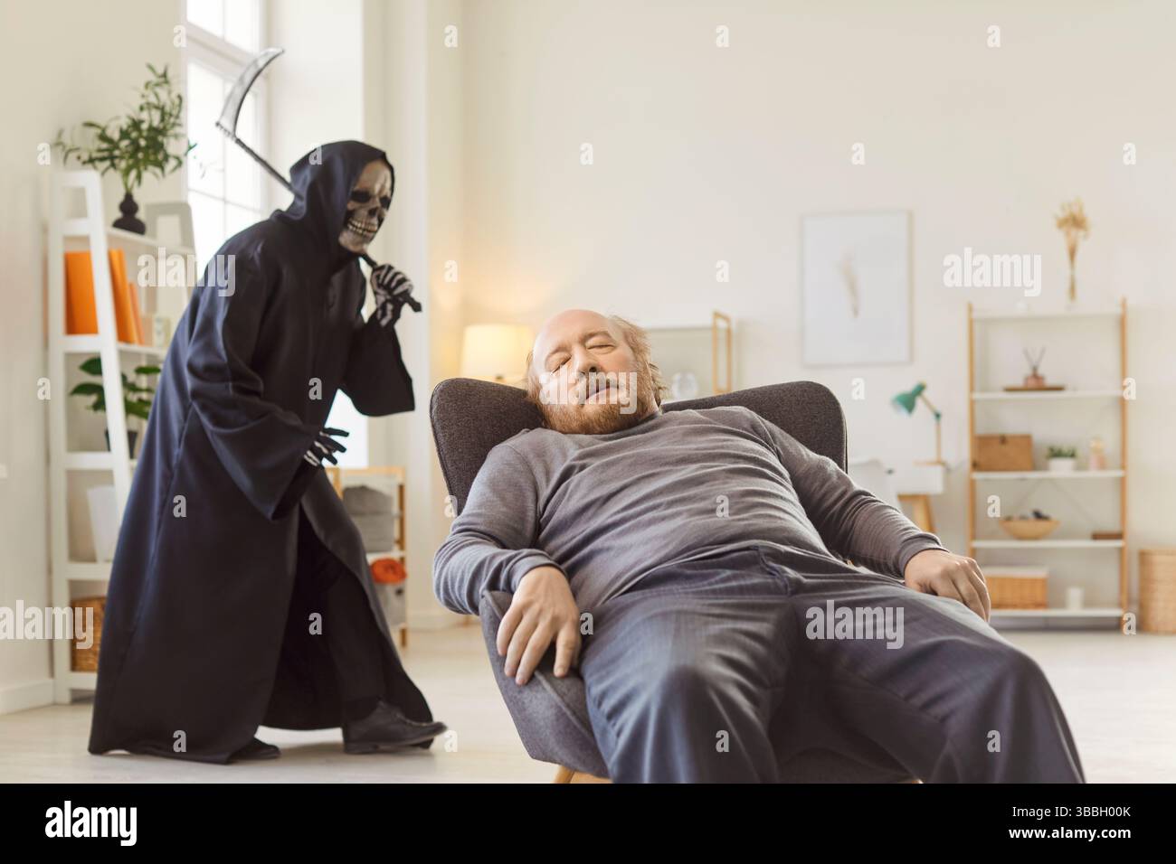 Bewusstloser Seniorenmann sitzt zu Hause mit dem Tod, der Sense hält, die hinter ihm läuft Stockfoto