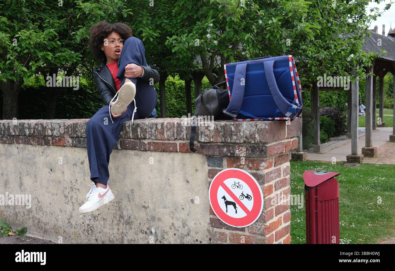 Ein französischer Schüler sitzt an der Wand und wartet auf den Transport nach der Schule in Frankreich Stockfoto