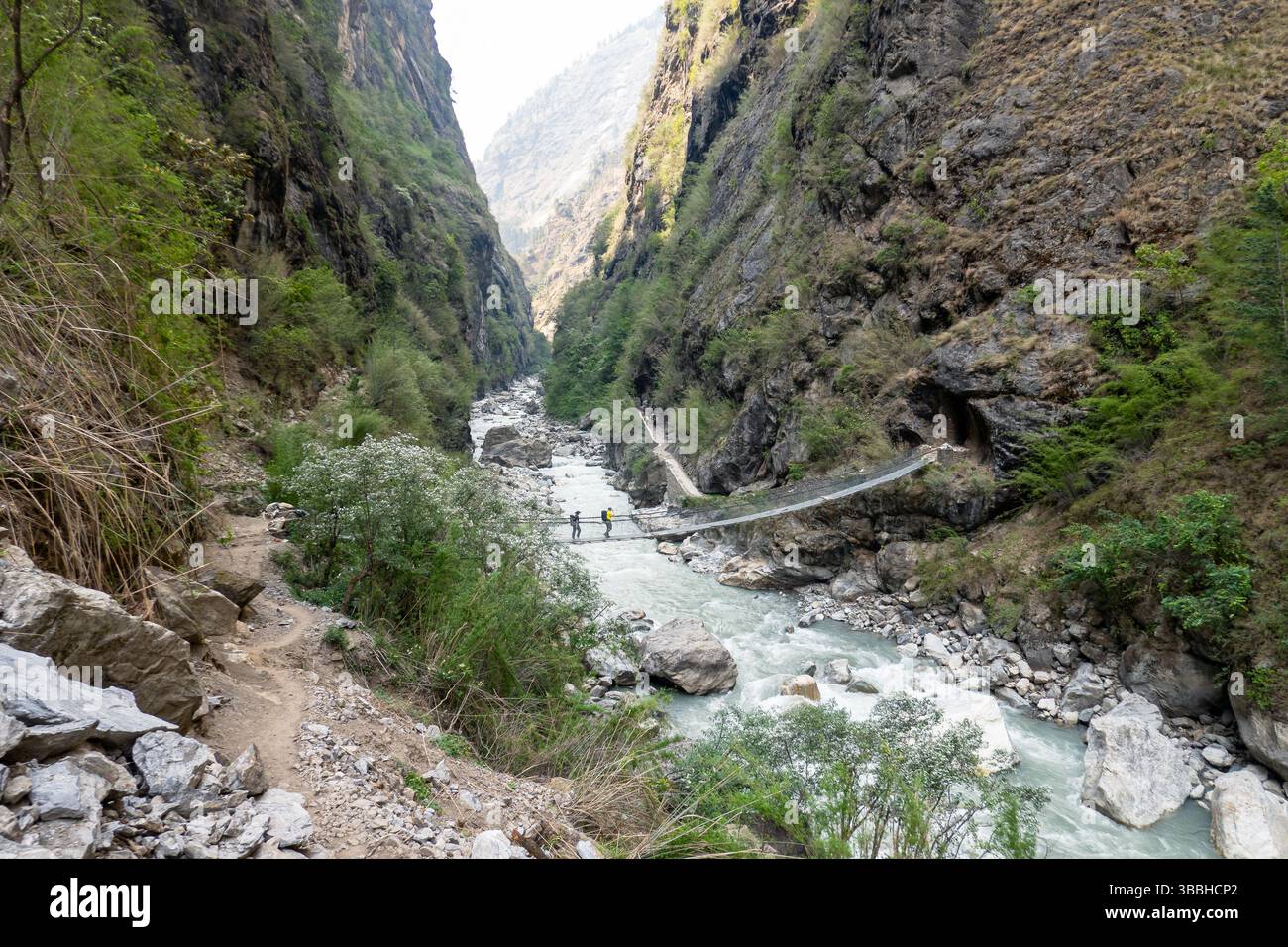 Trekker überquert eine Hängebrücke über einen Bergfluss in einer tiefen Schlucht entlang des unteren Abschnitts des Manaslu Circuit in Nepal Stockfoto