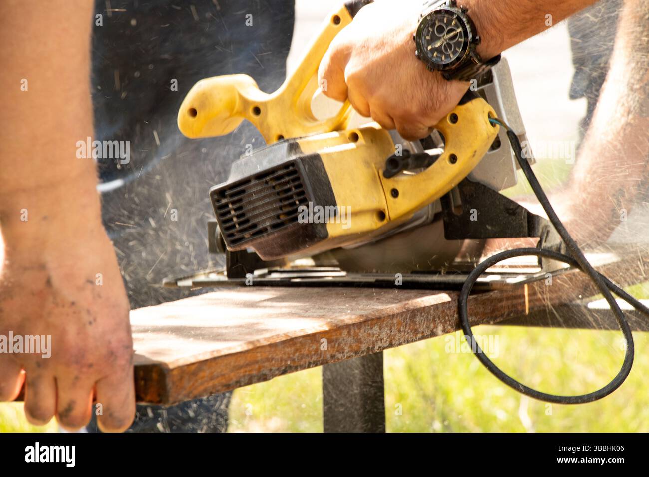 Ein Mann sägt ein Brett mit einer Kreissäge auf einem Tisch draußen und Sägemehl verschüttet, sägt ein Brett Stockfoto