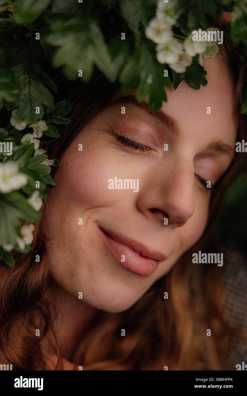 Eine ruhige Frau umgeben von grünen Blättern und Blumen Stockfoto