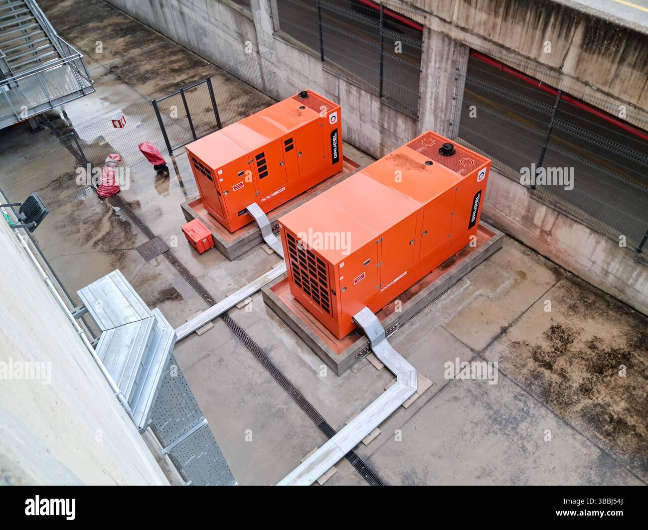 Zwei orangefarbene industrielle Dieselgeneratoren, die Notstrom in einer Betoneinhausung bereitstellen Stockfoto