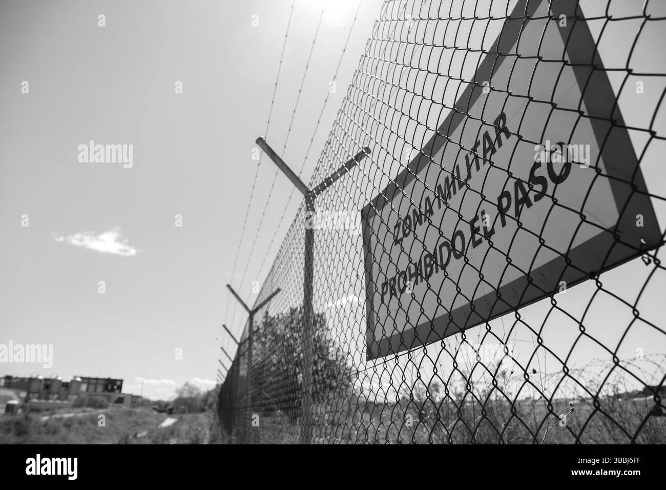 Übersetzung: "Militärzone, kein Zutritt." Stacheldrahtzaun verhindert den Zugang zu einer Einrichtung Stockfoto
