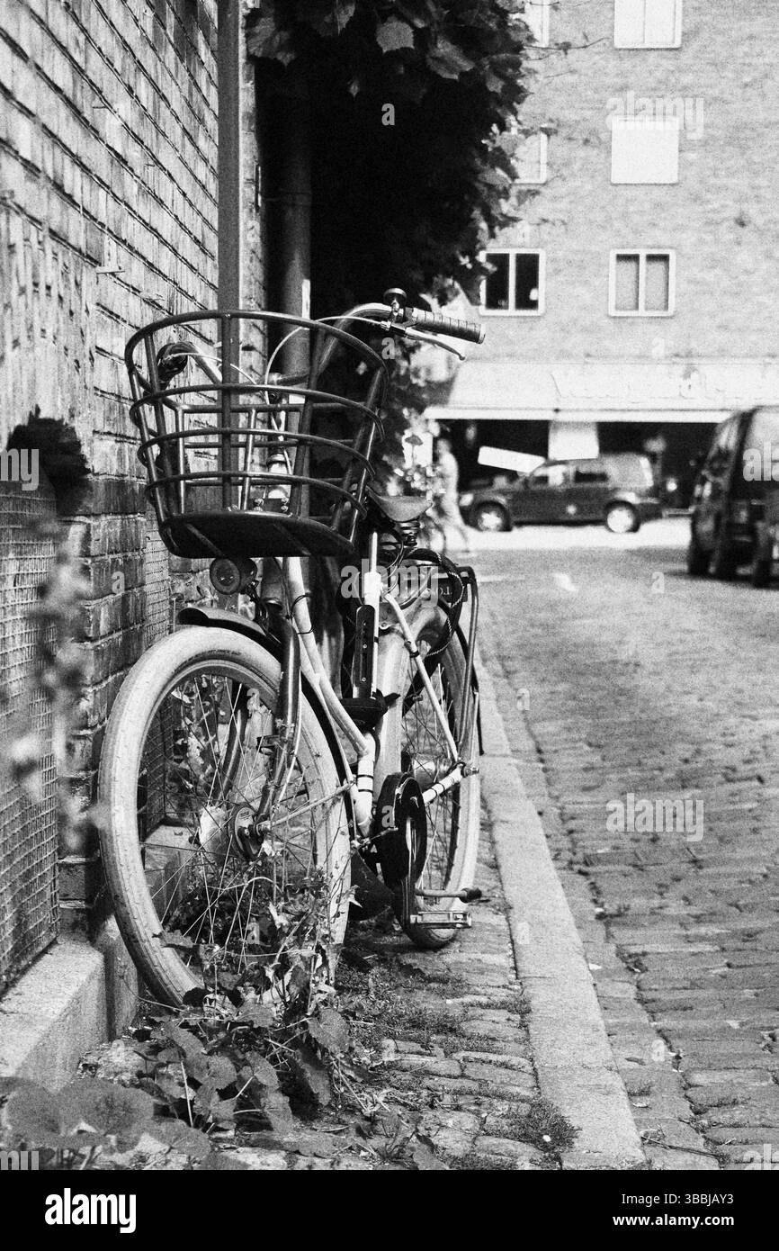 Vintage-Fahrrad mit Korb vor einer Backsteinmauer in einer Kopfsteinpflasterstraße, Schwarzweißfoto. Stockfoto