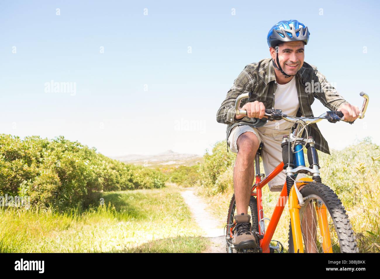 Radfahrer, der Fahrrad auf dem Feldweg mit orangem Rahmen, blauem Helm, Wasserflasche, Kopierraum in die Pedale tritt Stockfoto