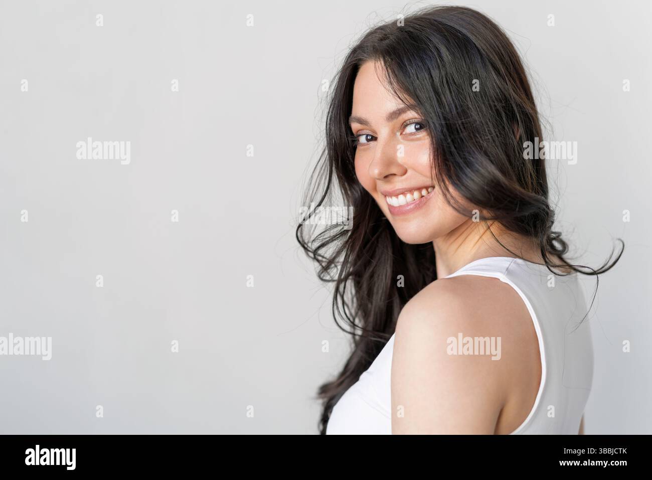 Schöne lächelnde Frau mit langen dunklen Haaren, die auf weißem Hintergrund posiert Stockfoto