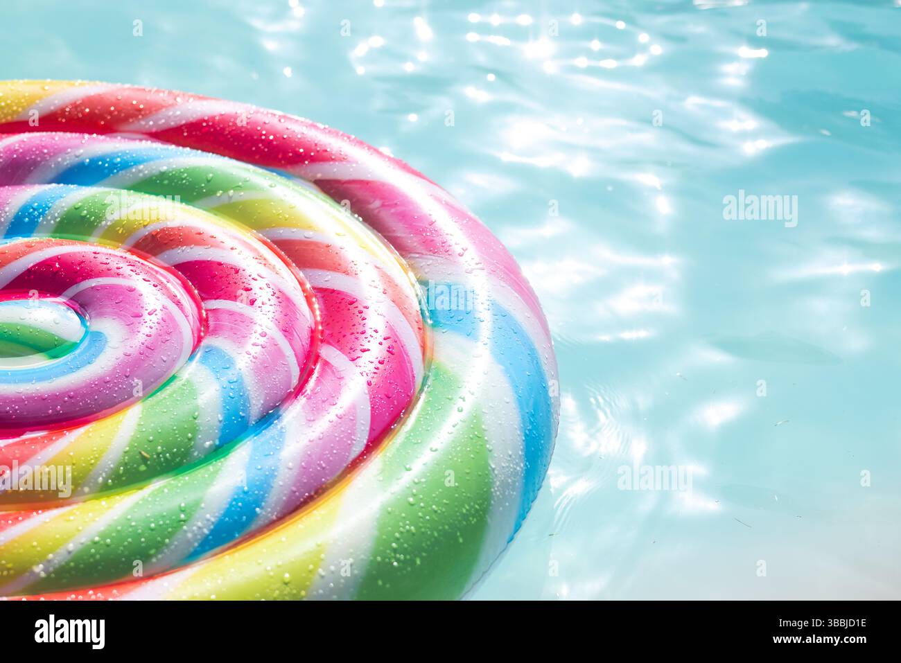 Der spiralförmige Pool mit Regenbogenstreifen schwimmt in türkisfarbenem Wasser mit Tropfen unter hellem Sonnenlicht Stockfoto
