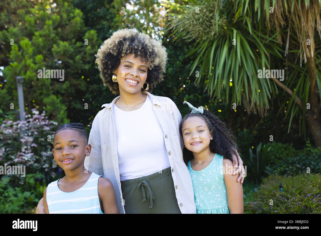 Lächelnde afroamerikanische Mutter umarmt den Sohn, Tochter im üppigen Garten, feiert Familienbindung Stockfoto
