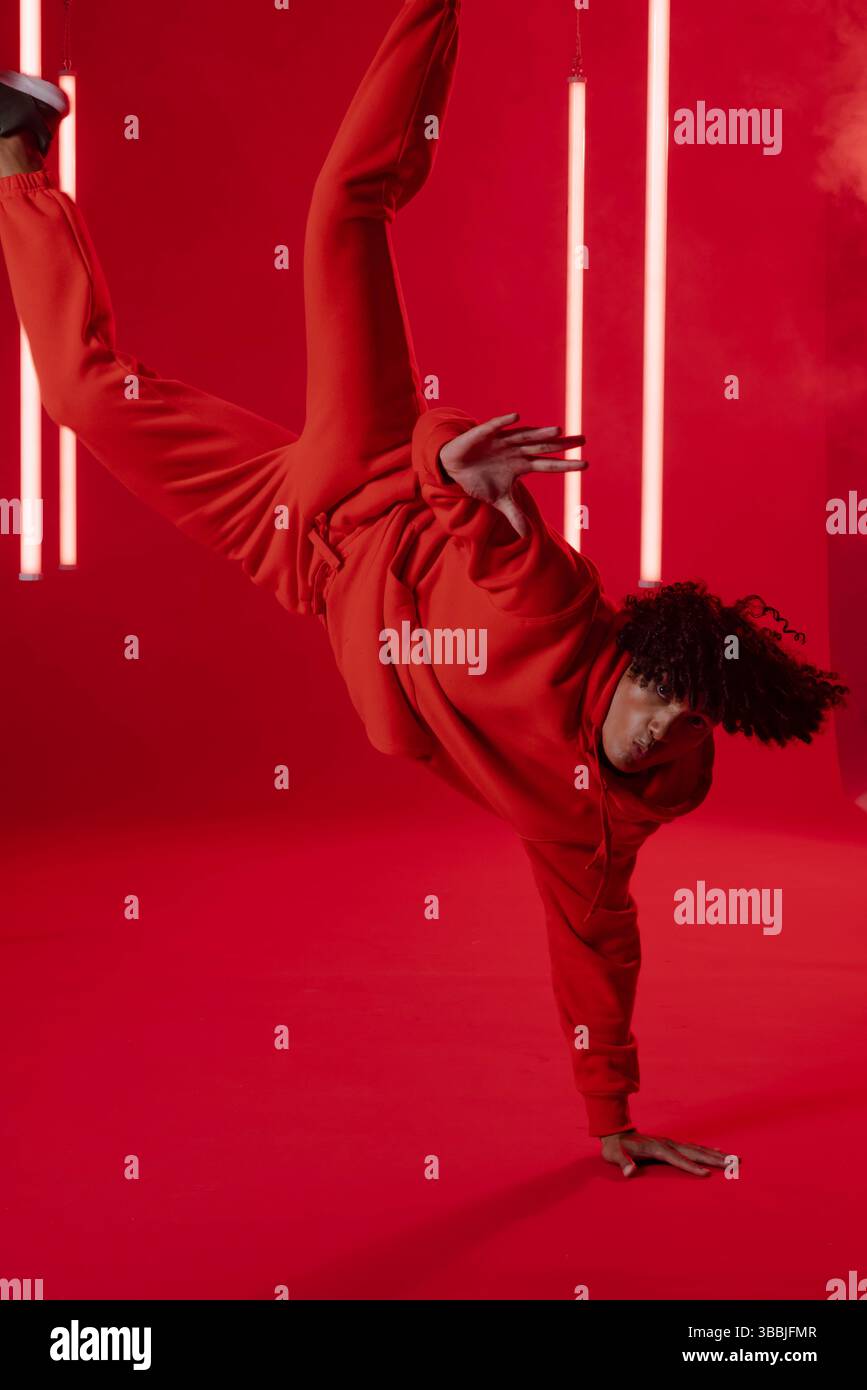 Ausbalancierender männlicher Tänzer, der einen Handstand im roten Studio macht, mit LED-Röhrenlichtern und Rauchnebel Stockfoto