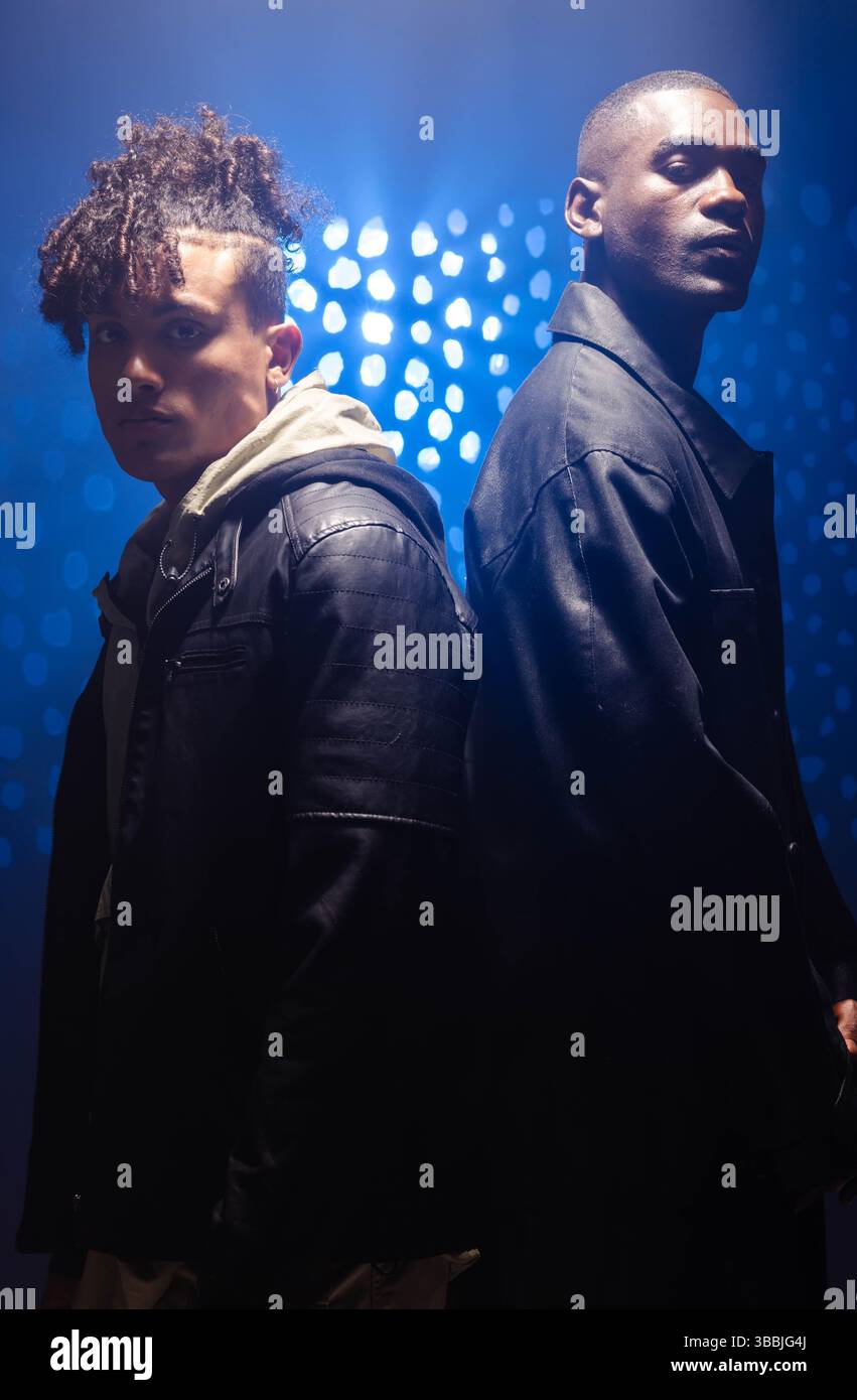 Verschiedene männliche Freunde in Lederjacke, die im blau beleuchteten Studio hintereinander stehen Stockfoto