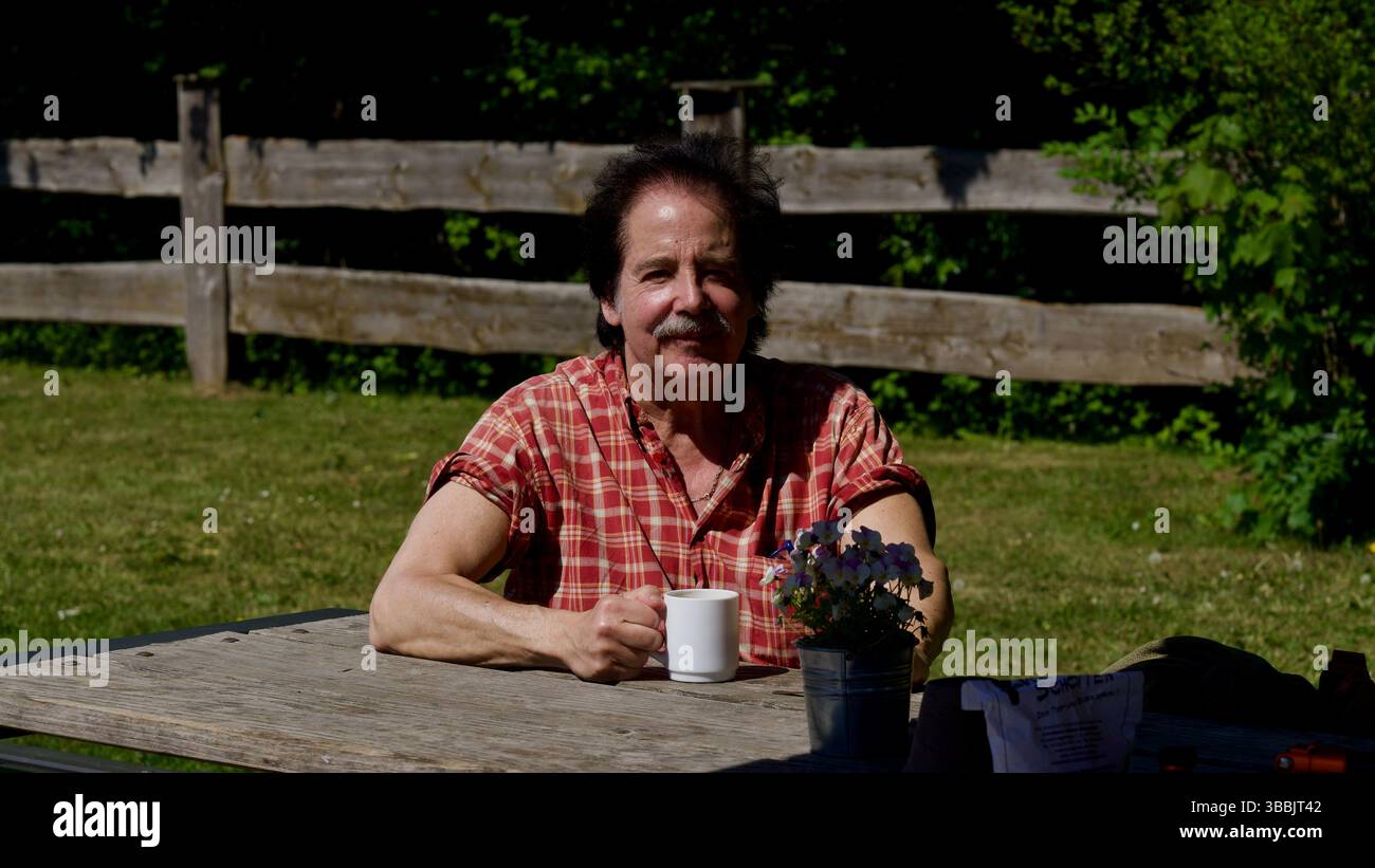 Attraktiver Mann, der eine Tasse Kaffee in einem Park in der Sonne hält. Stockfoto
