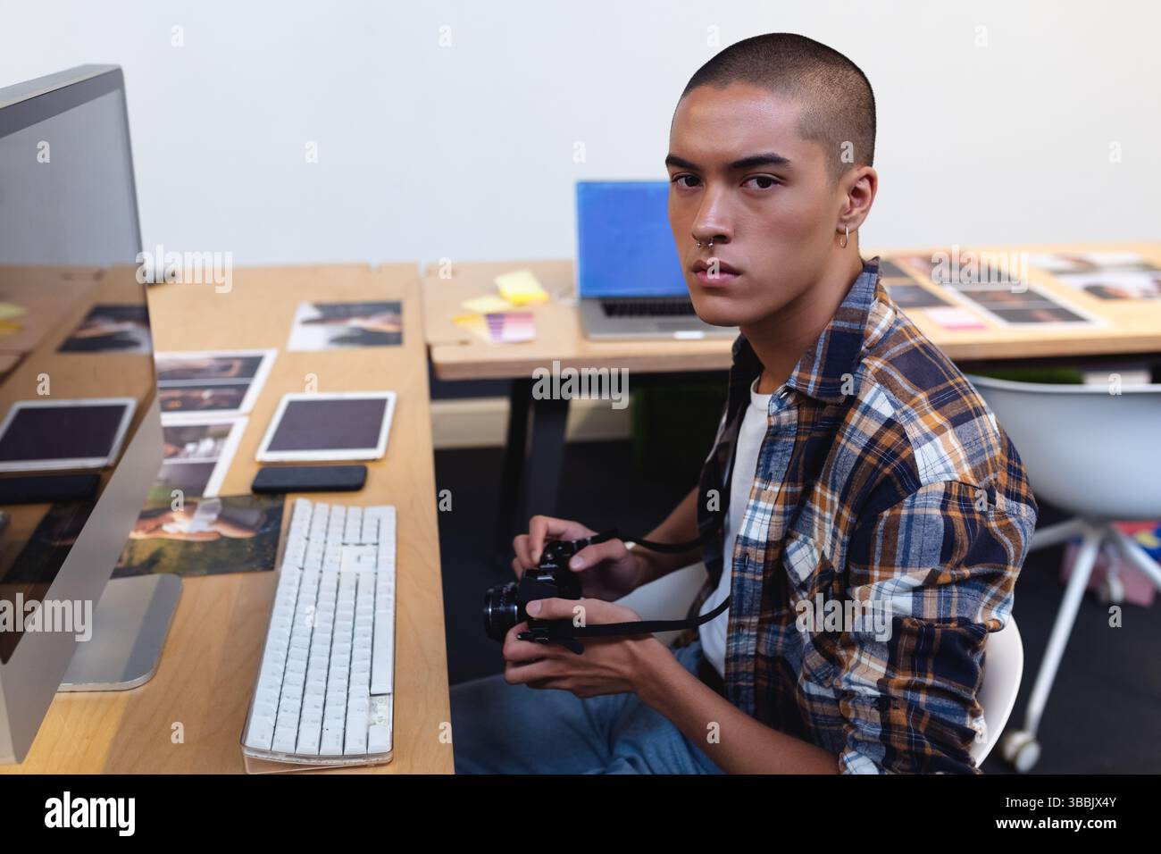 Bearbeitungsmann sitzt am Holzschreibtisch im Studio-Arbeitsbereich, mit DSLR-Kamera und Fotos, Kopierraum Stockfoto