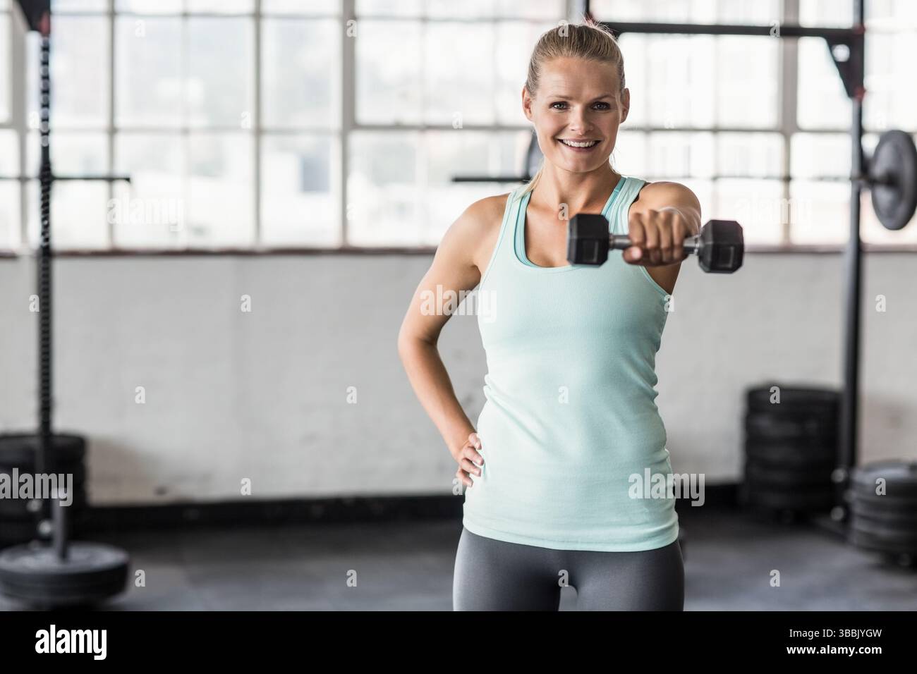 Hantel heben, Frau, die Schulterheben im Fitnessstudio mit Gitterfenstern, Stärke zeigt Stockfoto