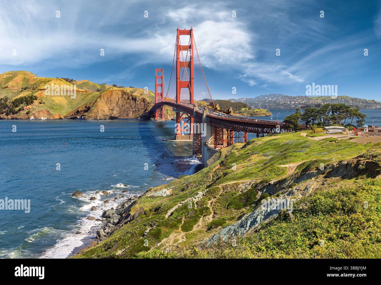 Die legendäre Golden Gate Bridge erstreckt sich über eine lebhafte blaue Bucht unter einem teilweise bewölkten Himmel mit üppigen grünen Hügeln, die das Wasser umgeben. Ein landschaftlich reizvolles Pat Stockfoto