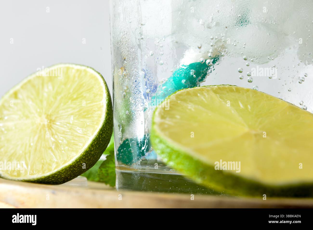 Detail der Glasbasis mit einem erfrischenden Getränk mit Strohhalm und Eis und Limetten- und Minzscheiben. Vorderansicht. Stockfoto