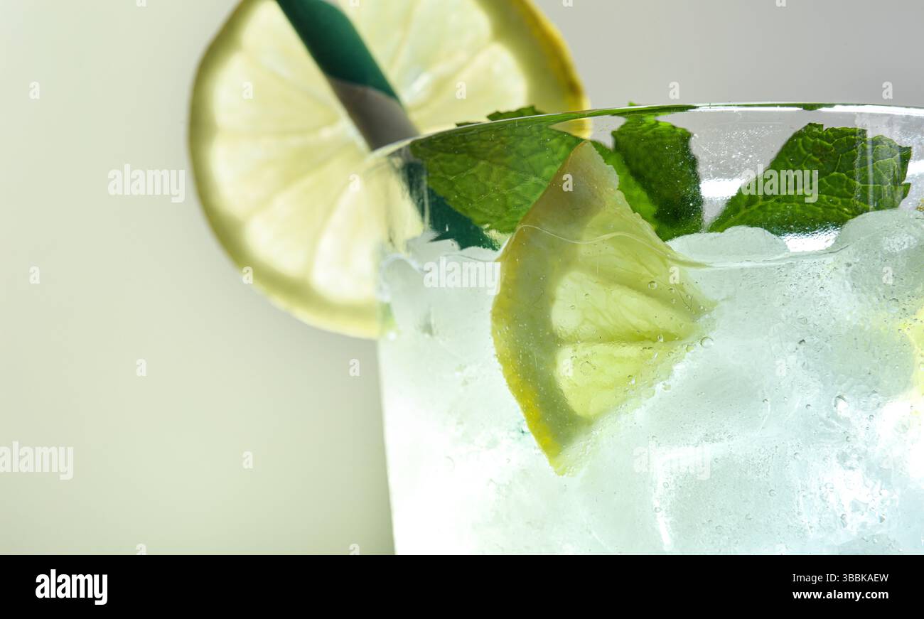Glasbecher mit erfrischendem Getränk mit Eis dekoriert mit Minze und Zitrone und grünem und weißem Stroh mit isoliertem Hintergrund. Vorderansicht. Stockfoto