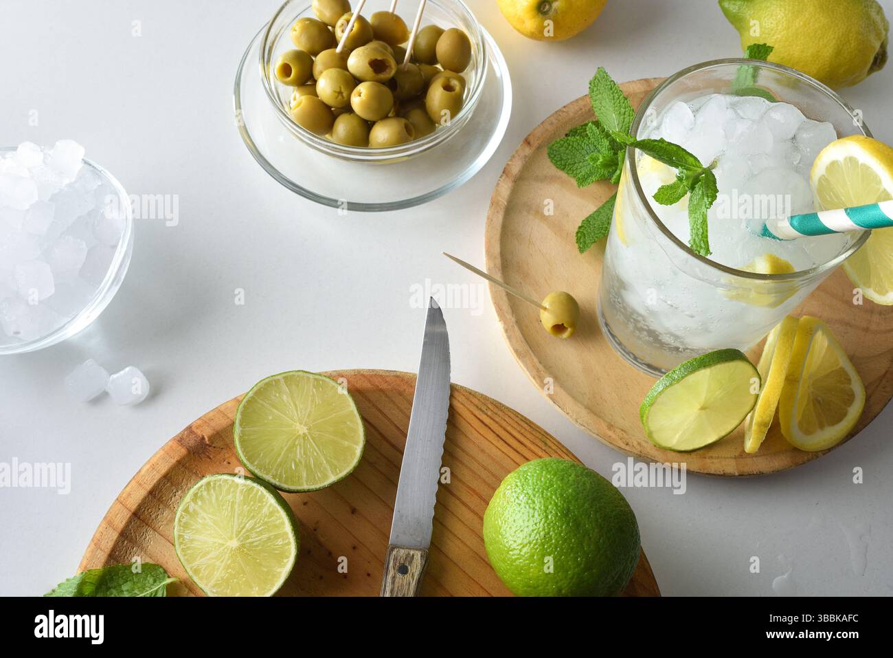 Küchenzeile mit erfrischendem Getränk auf Basis von Minze, Zitrone und Limette, mit Schneidebrett und Obst und Behältern mit Eis und Oliven. Draufsicht. Stockfoto