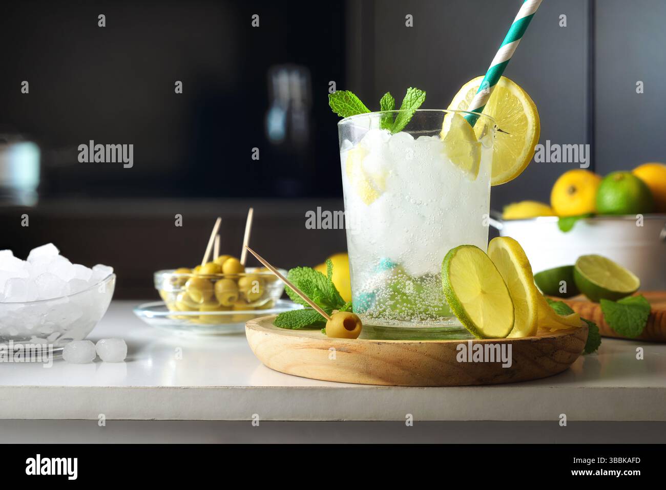 Küchenzeile mit Glasbecher mit Zitronen-, Limetten- und Minzsaft-Getränk mit Behältern mit Eis und Snacks und Hintergrund mit dunkler Küche. Vorn V Stockfoto
