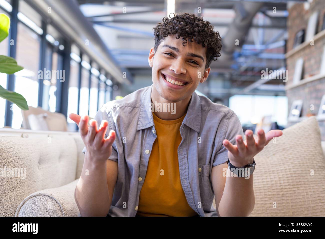 Junger Erwachsener, der auf einem beigefarbenen Sofa mit Topfpflanzen und Armbanduhr in der modernen Bürolounge sitzt Stockfoto