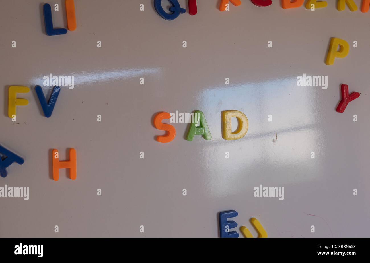 Bunte magnetische Buchstaben „traurig“ auf einem Whiteboard mit Holzrahmen im Klassenzimmer oder im Spielzimmer. Stockfoto