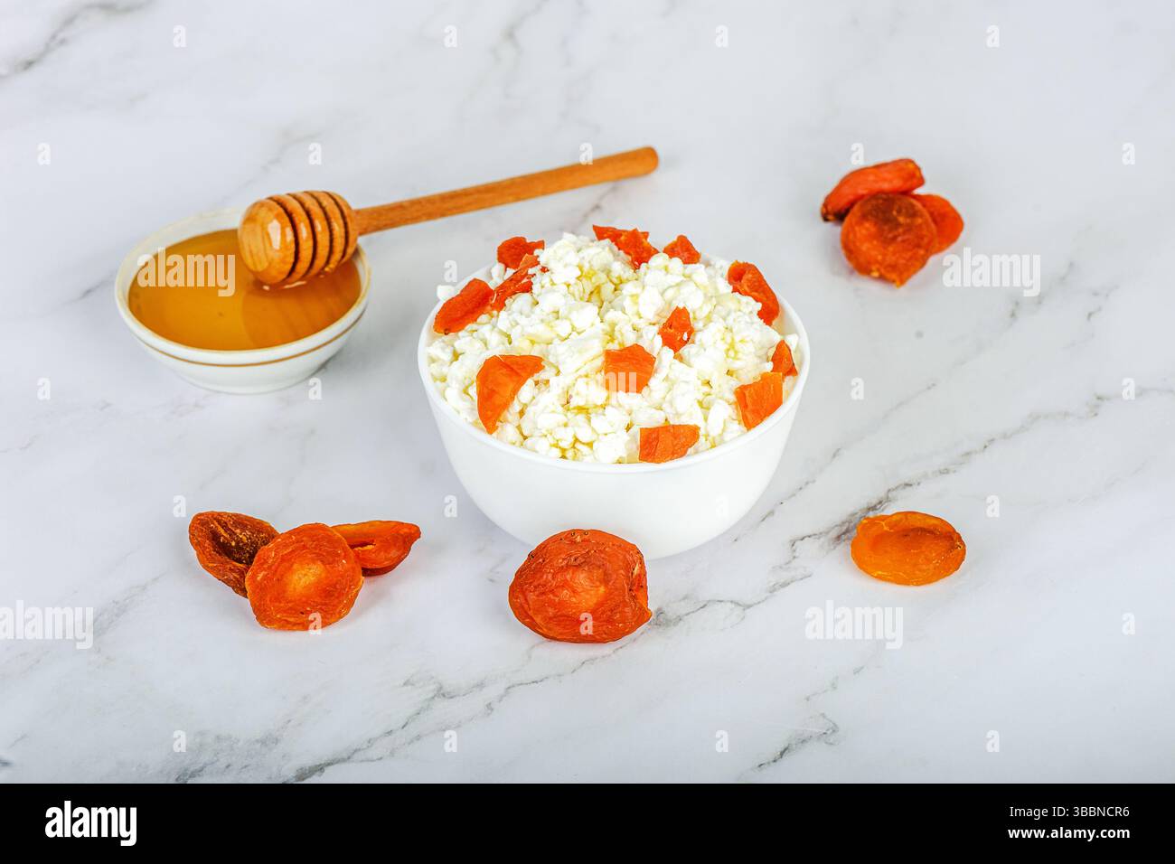 Frischer Hüttenkäse mit getrockneten Aprikosen und Honig in einer weißen Schüssel und Zutaten rund um die Schüssel. Gesunde Ernährung. Stockfoto