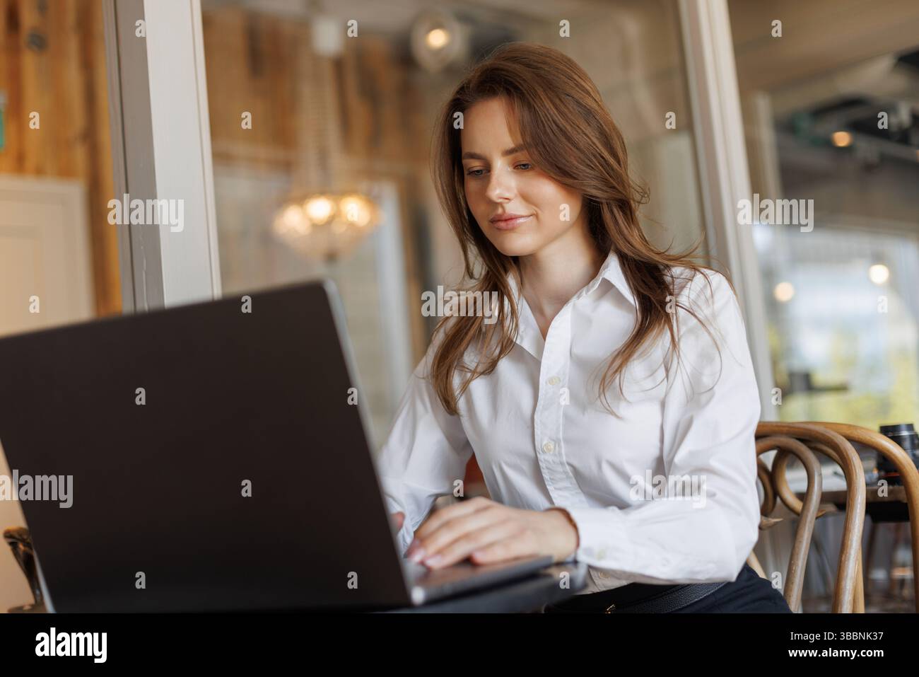 Fokussierte Frau im Smart Casual Outfit, die an Einem Café-Tisch arbeitet. Praktischer Laptop, Kaffee In Der Nähe – Perfekte Kulisse Für Digitales Unternehmertum Und Stockfoto
