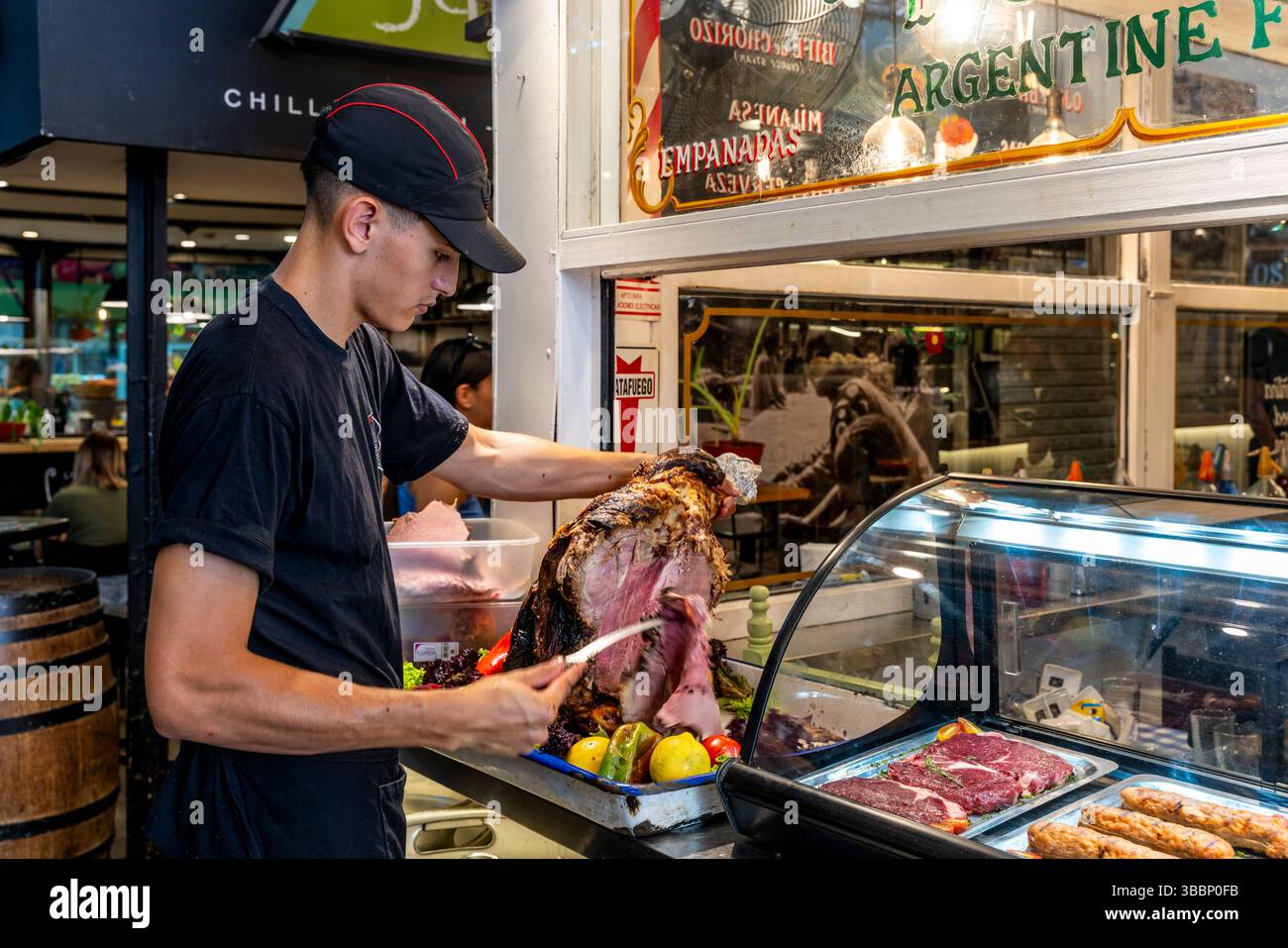 Ein junger Mann, der Rindfleisch in Einem Café im Mercado de San Telmo, San Telmo, Buenos Aires, Argentinien schnitzt. Stockfoto Ein junger Mann, der Rindfleisch in Einem Café im Mercado de San Telmo, San Telmo, Buenos Aires, Argentinien schnitzt. Stockfoto