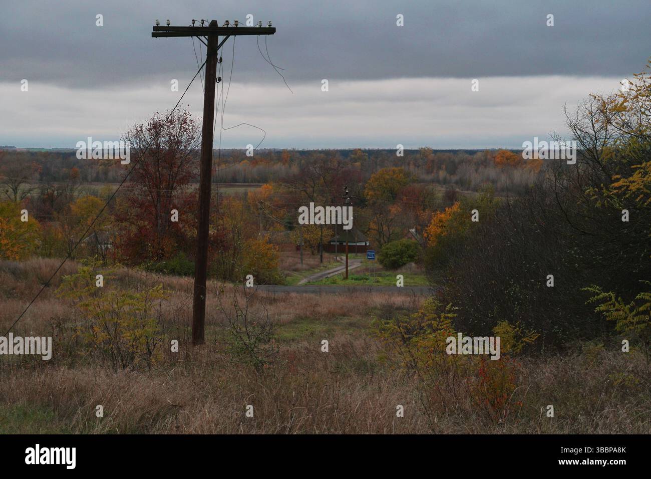 Alte alte Holzmaste mit gerissenen Drähten vor stürmischem Himmel in herbstlicher Landschaft Stockfoto