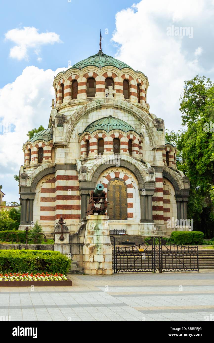 Diese beeindruckende architektonische Struktur verfügt über abwechselnde rote und weiße Streifen und Kuppeln. Es liegt in einem ruhigen Park mit grünen Bäumen und farbenfrohen Bäumen Stockfoto