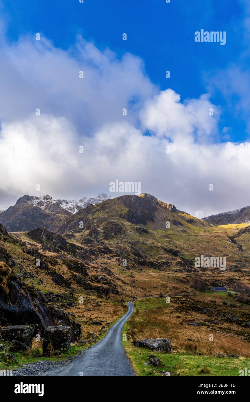 Eine gewundene Asphaltstraße durch das Gletschertal von Cwm Idwal führt zu zerklüfteten Snowdonia-Gipfeln unter einer dynamischen Wolkenlandschaft Stockfoto